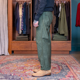 Person wearing  ORSLOW GREEN FATIGUES green pants standing in a room with wooden wardrobe and colorful rug