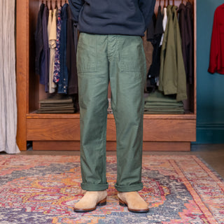 Person wearing green ORSLOW FATIGUES pants standing in AUTEUR STORE be and colorful rug.
